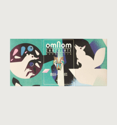 Omnom's milk and cookie bar on a grey background. The packaging is teal, black, and white, with bits of light pink. There are two artic foxes on the front
