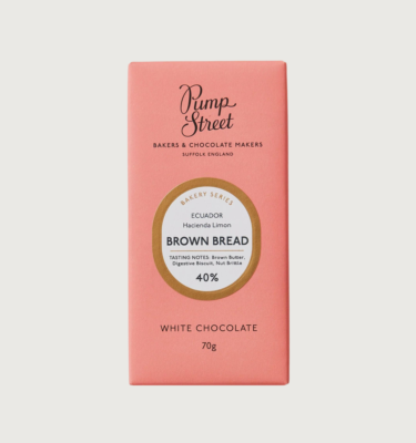 Picture of pump streets brown bread bar on a grey background. The packaging is pink, with a gold circle trim around the label