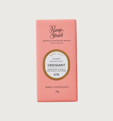 picture of pump streets croissant bar on a grey background. The packaging is pink with a gold circle around the label