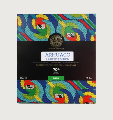 Chocolate tree's Arhuaco bar on a grey background. The packaging is red, yellow, light blue and, dark blue, and depicts two parrots of different colours circling around each other.