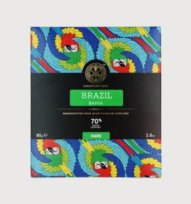 Picture of chocolate tree's brazil bahia dark bar on a grey background. The packaging is red, yellow, light blue and, dark blue, and depicts two parrots of different colours circling around each other.