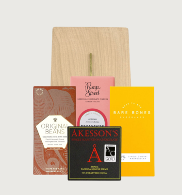 Picture of our dark chocolate sharing board on a grey background. The sharing board is a light beige colour, and there are four bars arranged in a diamond shape in front of it.