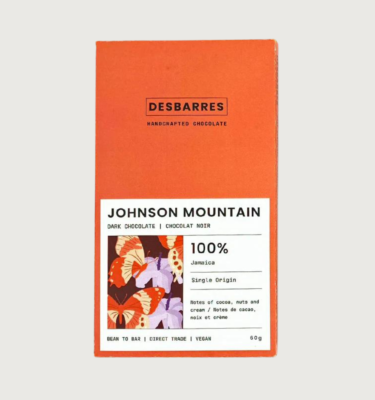 Desbarres 100% johnson mountain bar on a grey background. The packaging is a burnt orange colour, with a white label that has a small square of an lilac, burnt orange, orange and dark purple geometric pattern.