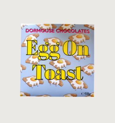 Picture of dormouse's egg on toast bar on a grey background. The packaging is a light blue, with cartoon eggs on toast in the back. The writing is bold and yellow.