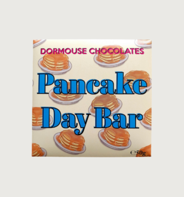 Picture of Dormouse's Pancake day bar on a grey background. The bar is square, and the packaging is white with cartoon pancakes in the background, and bold blue writing.