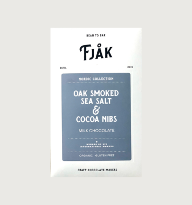 Picture of fjak's oak smoked sea salt and cocoa nibs milk bar on a grey background. The bar is white, with a bluey grey label in the centre.