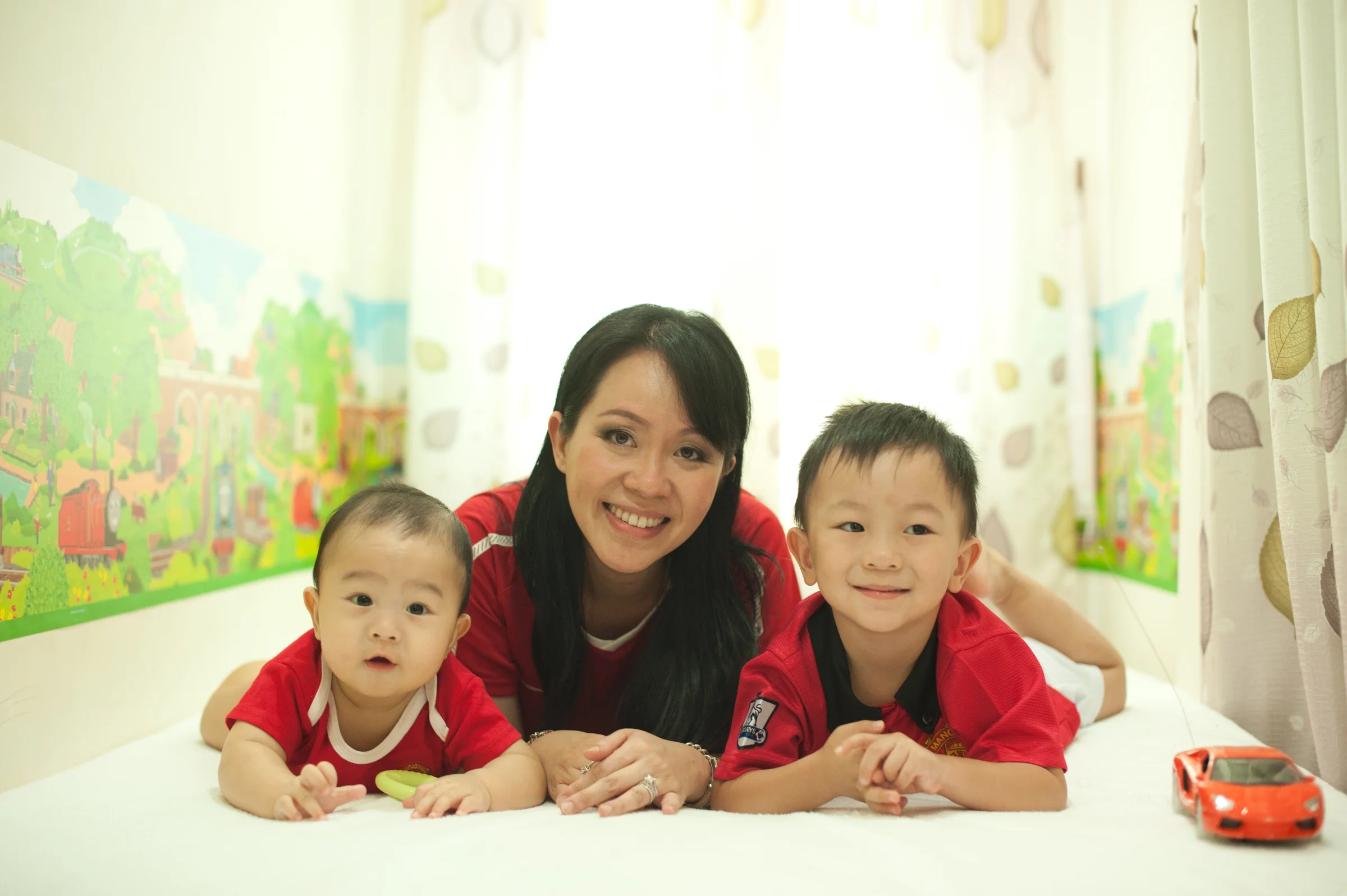 A photo of a woman with brown hair with two young boys either side of her with brown hair too. They're lying down on their stomachs and smiling at the camera.