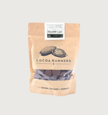 Original beans' 62% milk couverture in a 230g bag on a grey background. The bag is a light tanned brown, with a black sketch of cocoa pods just above the cocoa runners logo. There is a gap in the packaging which has been replaced with clear plastic, so you can see the buttons.