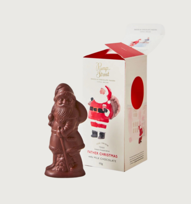 Pump street's father christmas on a grey background. The chocolate santa is posed with a sack on his back, and the open packaging behind him. The packaging is white and red, with a cartoon happy santa depicted on the front.