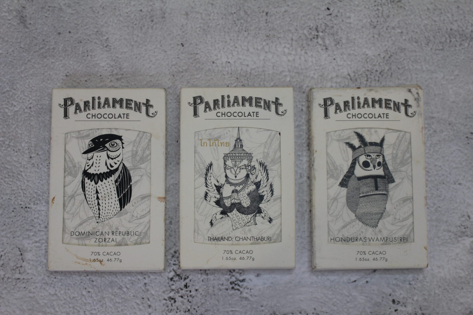 Picture of three of parliaments bars on a white marble table. The bars are white, with black illustrations and writing on them.