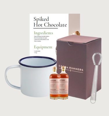 Spiked hot chocolate set on a grey background. There are two mini Arran Sherry's, our Cru Virunga hot chocolate powder, a small whisk, a white enamel mug with a blue ring, and a copy of the spiked hot chocolate letter.