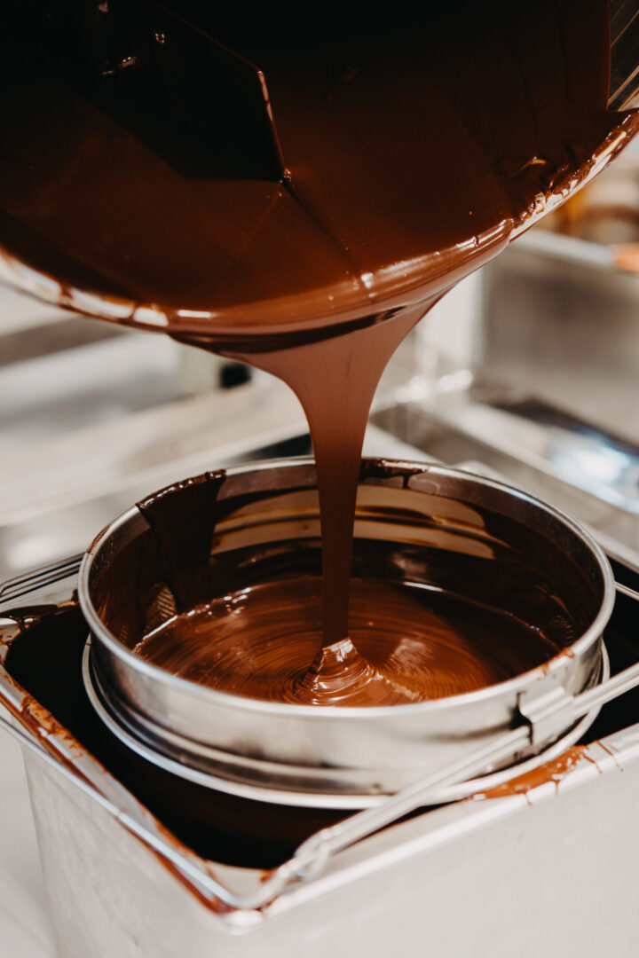 Melted chocolate being poured from one metal bucket into another.
