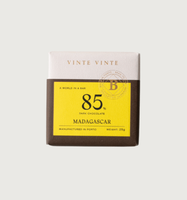 A photo of a Vinte Vinte dark chocolate minibar on a grey background. The packaging is white, yellow, and brown and the bar uses beans from Mava, Madagascar.
