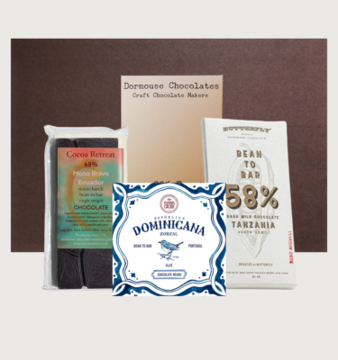Picture of our international womens day box on a grey background. There are four bars, arranged in front of a brown cocoa runners hamper