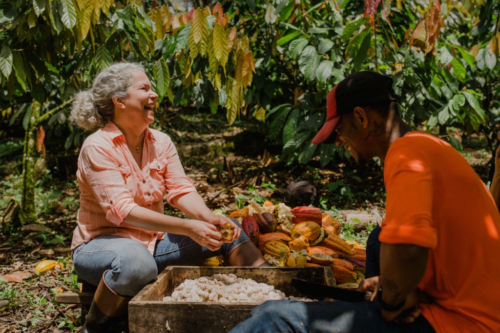 Picture of Juliana from Baiani and a collegue laughing while outside in the cocoa plantation, holding a cocoa pod.